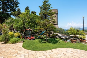 A garden with a stone tower, various trees, and a paved area with a lawn. - AMORE RENTALS - Villa Imma with Swimming Pool and Sea View (Castellammare di Stabia)