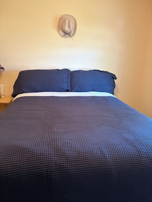 A bed with a textured blue blanket, a white pillow, and a wall-mounted light fixture. - 3 bedroom home with hot tub and garage in Hays, KS (Hays)