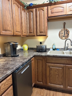 A kitchen with wooden cabinets, a dishwasher, a coffee maker, a toaster, and a sink with a faucet. - 3 bedroom home with hot tub and garage in Hays, KS (Hays)