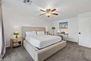 A hotel room with a single bed, a ceiling fan, a nightstand with a lamp, a desk with a chair, and a door. - Tonto Casita – Luxury Foothills Home w/ Mtn Views (Apache Junction)
