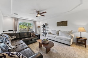 A living room with a dark leather sofa, a light-colored sofa, a coffee table, and a ceiling fan. - Tonto Casita – Luxury Foothills Home w/ Mtn Views (Apache Junction)