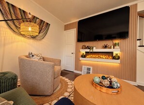 Una sala de estar moderna con un televisor de pantalla plana, una chimenea y una mesa de centro redonda de madera.