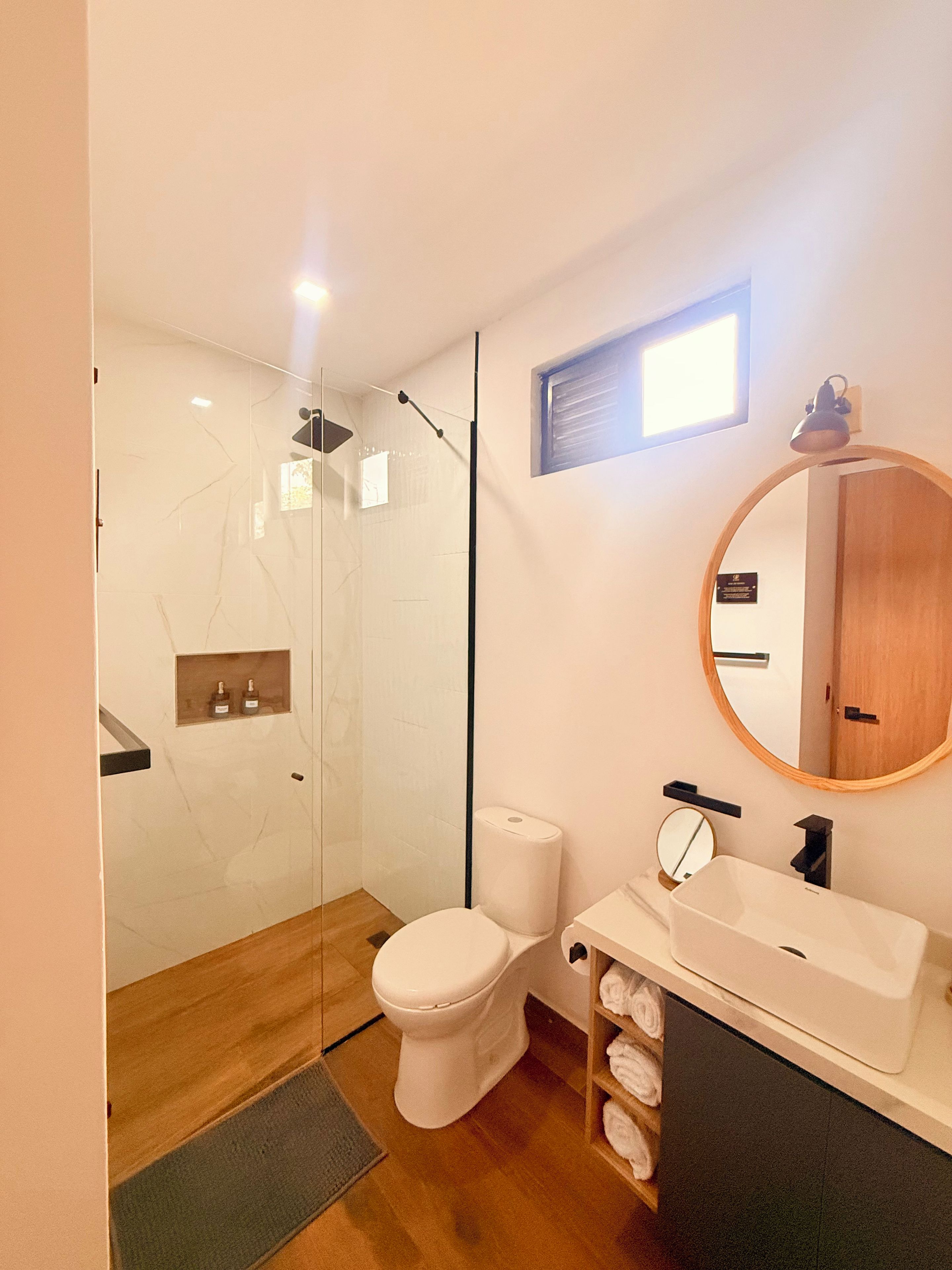 Un baño moderno con ducha envuelta en vidrio, inodoro y lavamanos con espejo.