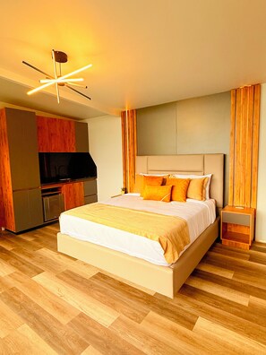 Une chambre d’hôtel moderne dotée d’un grand lit, d’un plancher en bois, d’un téléviseur intégré et d’une kitchenette.