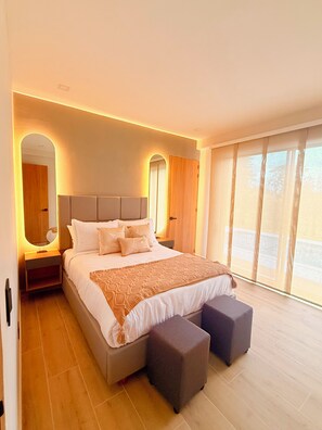 Un dormitorio moderno con una cama grande, mesitas de noche, un espejo y vistas amplias a través de grandes ventanales.