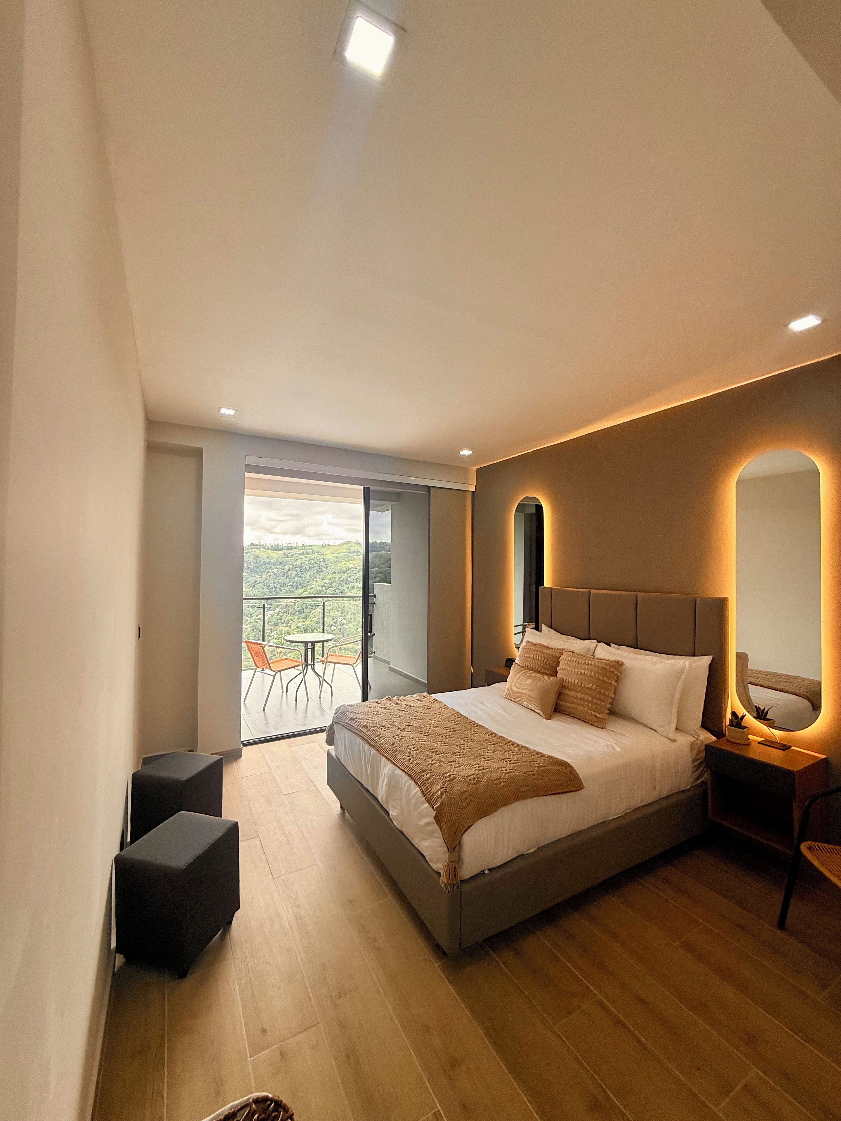 A modern bedroom with a large bed, a bedside table, a chair, and a balcony with a view.