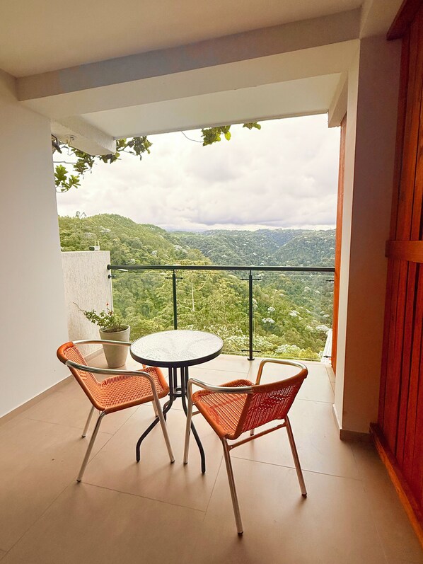 Un balcon agrémenté de deux fauteuils en osier et d’une petite table, offrant une vue sur un paysage verdoyant et luxuriant.