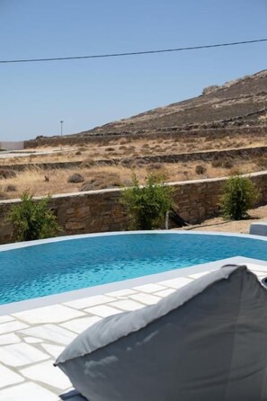 Una piscina con un muro de piedra y una colina cubierta de césped al fondo.