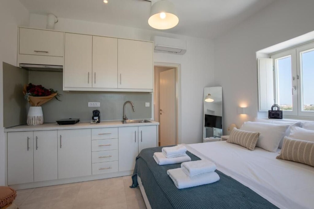 Una habitación de hotel moderna con una cama, una pequeña kitchenette y un ventanal con vistas.