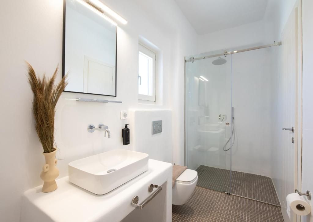 Un baño moderno con lavamanos blanco, un espejo, inodoro y cabina de ducha con mampara de vidrio.