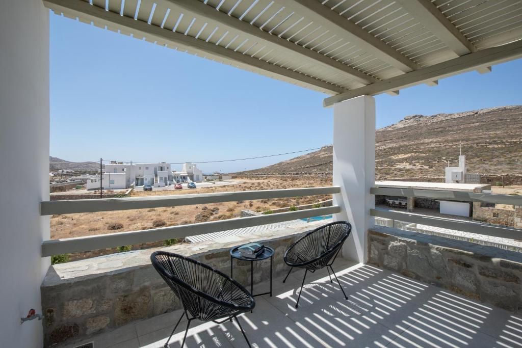 A balcony with two chairs, a table, and a view of a building and landscape.