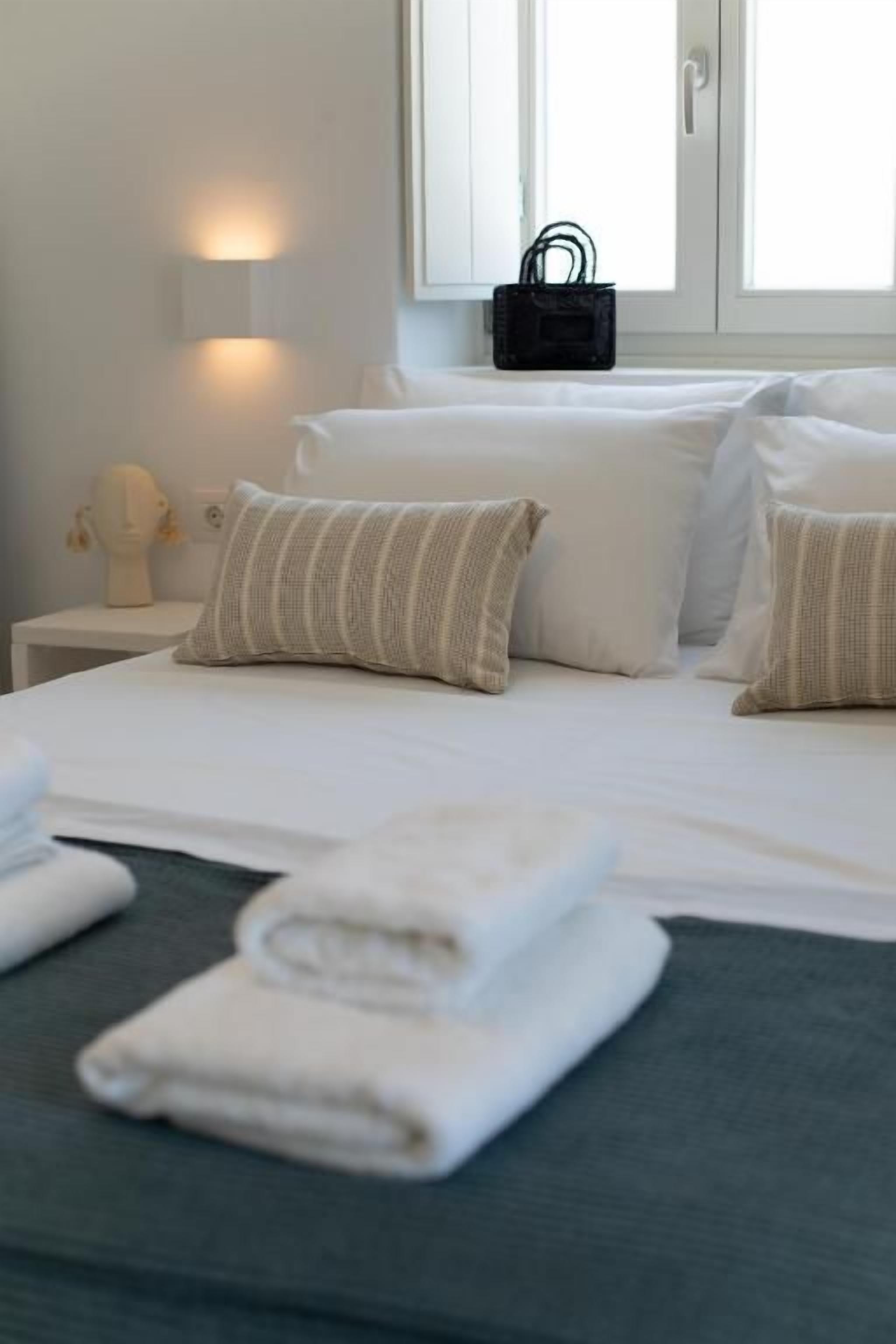 Une chambre d’hôtel avec un lit, des oreillers, une table de chevet, une lampe et une fenêtre sur le rebord de laquelle est accroché un sac.