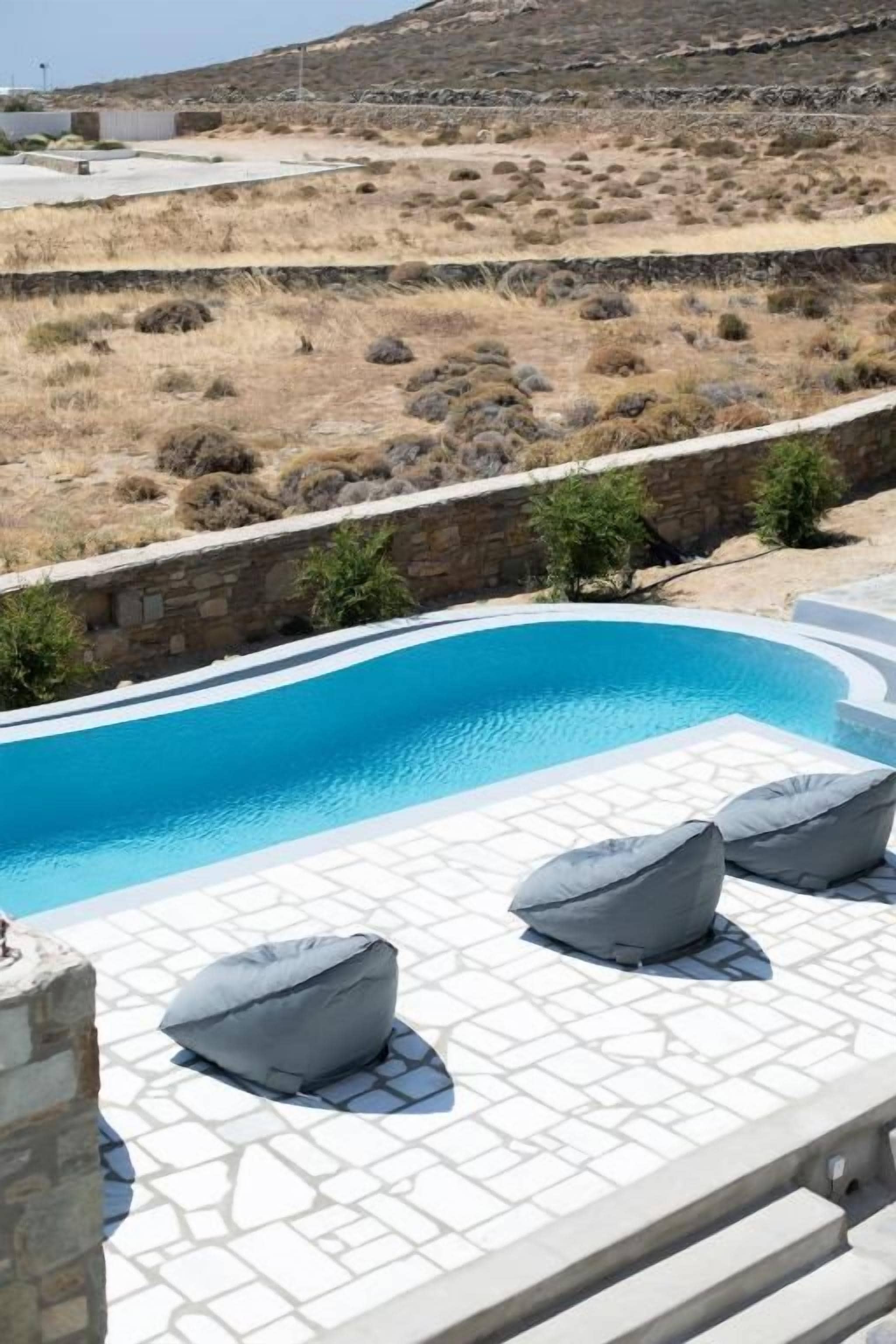 Una piscina con solárium de piedra y sillones de descanso.