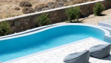 Una piscina con solárium de piedra y sillones de descanso.