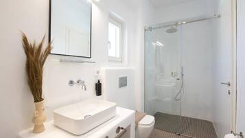 Un baño moderno con lavamanos blanco, un espejo, inodoro y cabina de ducha con mampara de vidrio.