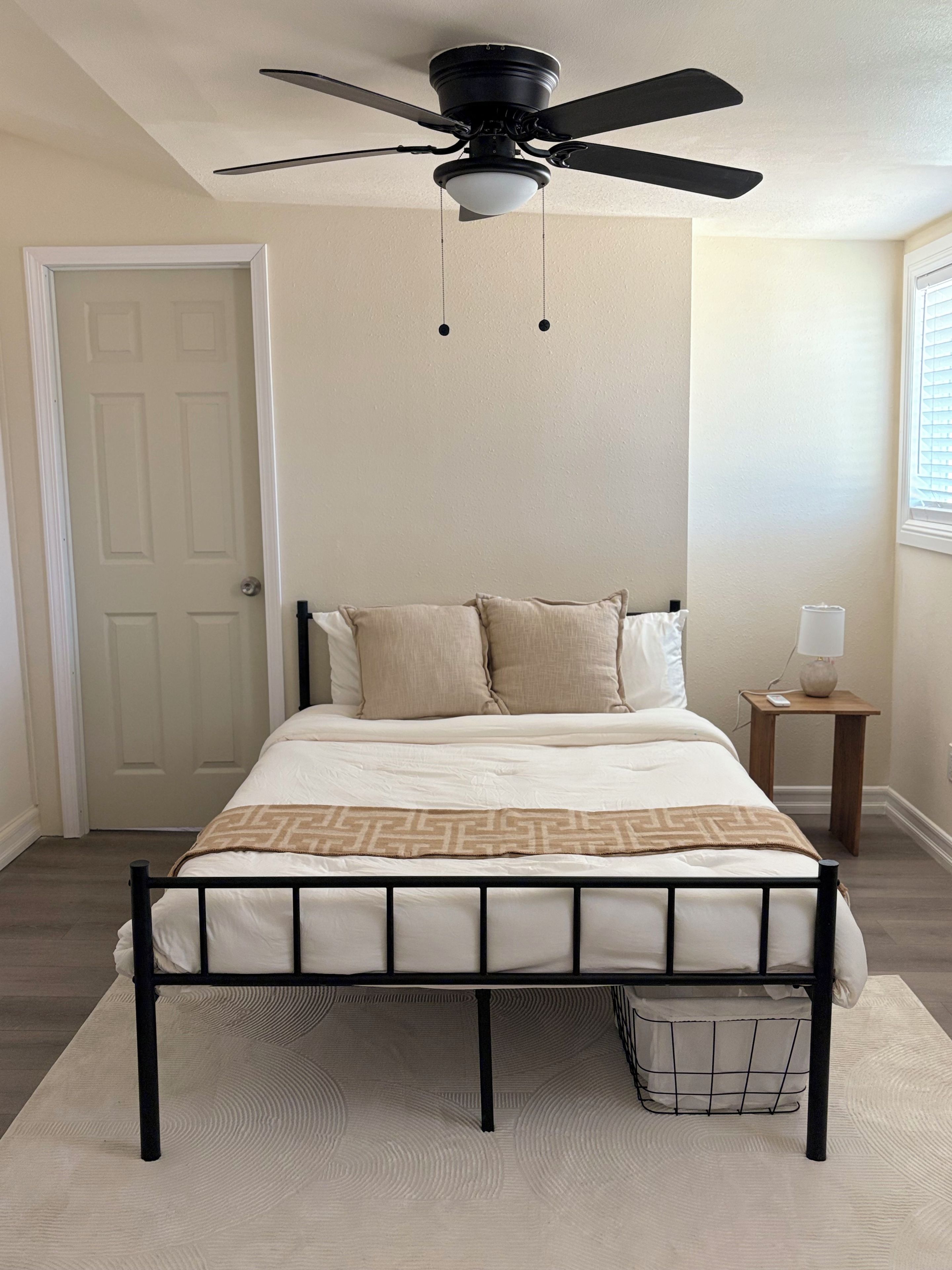 Une chambre à coucher avec un lit, un ventilateur de plafond, une table de chevet avec une lampe et une porte.