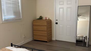 Une chambre à coucher comprenant un lit, une commode, un ventilateur de plafond, une fenêtre avec des stores, une porte et un miroir.