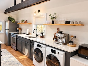 Cozinha moderna com eletrodomésticos de aço inoxidável, forno embutido, máquina de lavar e cafeteira.