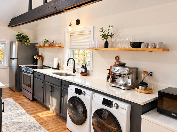 A modern kitchen with stainless steel appliances, a built-in oven, a washing machine, and a coffee machine. - Maple Cabin w Sauna, Indoor Hot Tub, + Firepit (Greentown)