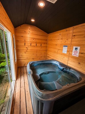 A wooden cabin with a hot tub, wooden walls, and a glass door leading outside. - Maple Cabin w Sauna, Indoor Hot Tub, + Firepit (Greentown)
