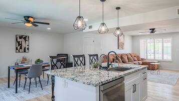 A modern kitchen with a central island, pendant lighting, and a dining area with chairs and a table.