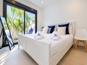 Ein modernes Schlafzimmer mit einem großen Bett, weißer Bettwäsche und Blick auf Grün.