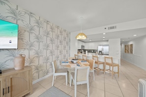 A modern kitchen with white cabinets, a central island, and a dining area with white chairs and a round table. - Heated Pool| Steps 2 Beach| King + Bunks| Kid Gear (Destin)