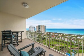 A balcony with a view of the ocean and buildings, furnished with chairs and a table. - Heated Pool| Steps 2 Beach| King + Bunks| Kid Gear (Destin)