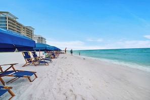 A beach with rows of blue beach chairs and umbrellas, a building in the background, and a clear sky. - Heated Pool| Steps 2 Beach| King + Bunks| Kid Gear (Destin)