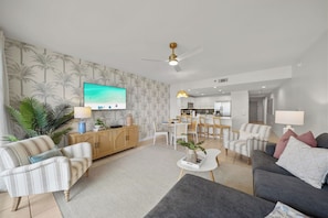 A modern living room with a television, sofa, and dining area. - Heated Pool| Steps 2 Beach| King + Bunks| Kid Gear (Destin)