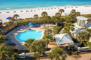 A resort with a swimming pool, beach chairs, umbrellas, and palm trees. - Heated Pool| Steps 2 Beach| King + Bunks| Kid Gear (Destin)