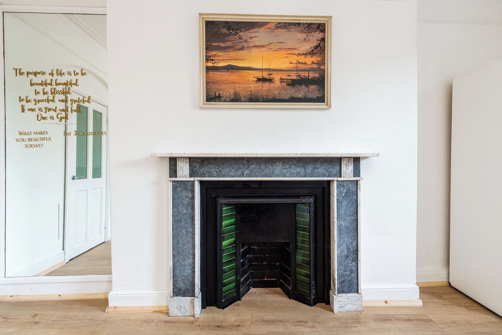 A room with a fireplace, a framed painting above it, and a door with a text message on the wall.