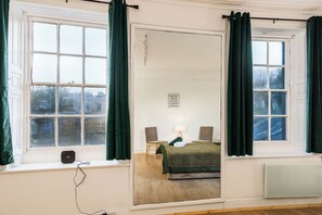 Een kamer met een bed, twee stoelen, een tafel met een lamp en een raam met gordijnen.