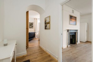 Ein Flur mit weißer Wand, Holzboden, weißer Tür und Kamin.