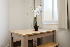 Ein Holztisch mit einer Orchidee in einem schwarzen Topf, platziert in der Nähe eines Fensters mit Vorhang.
