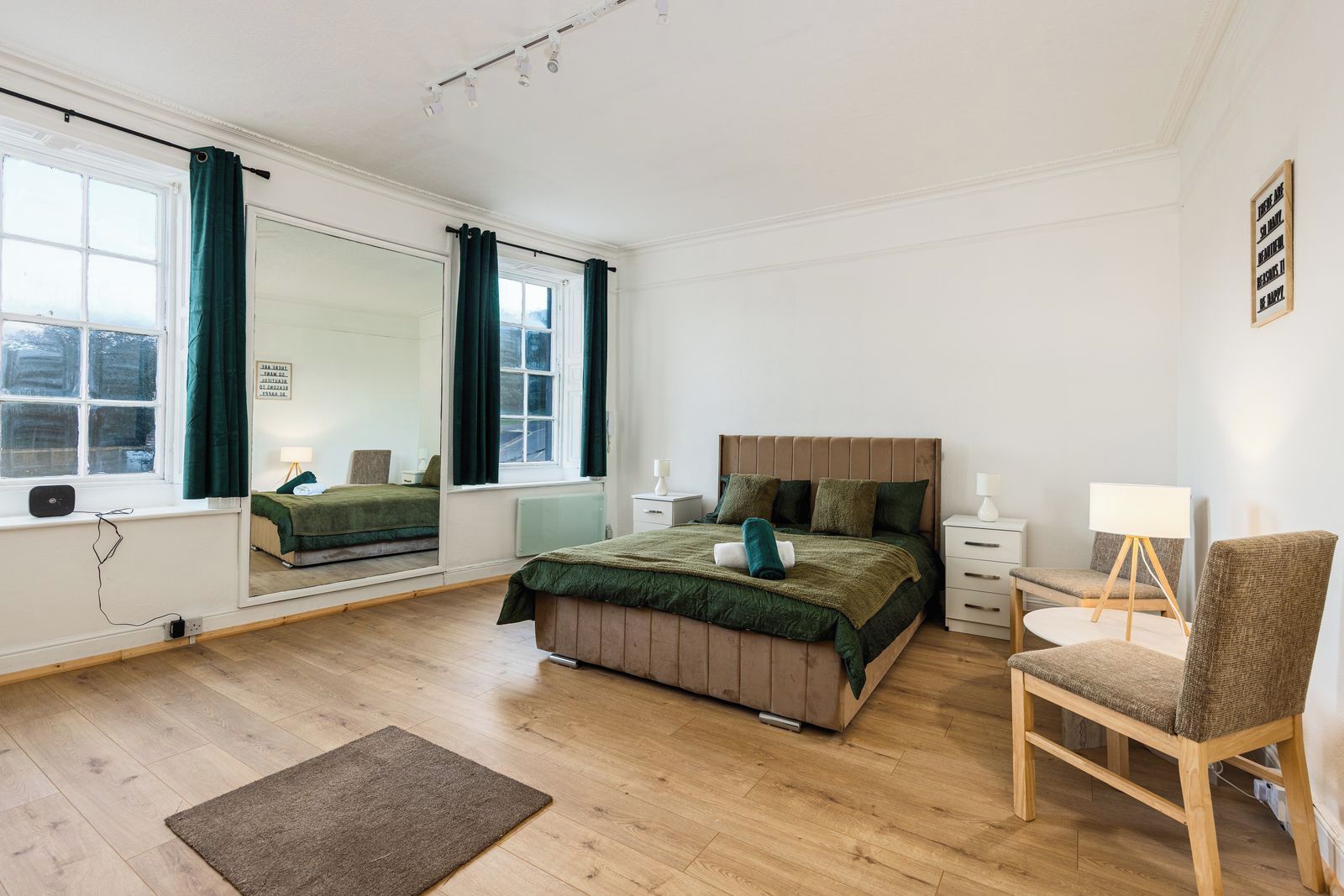 A bedroom with a bed, a chair, a desk, a mirror, and a window.