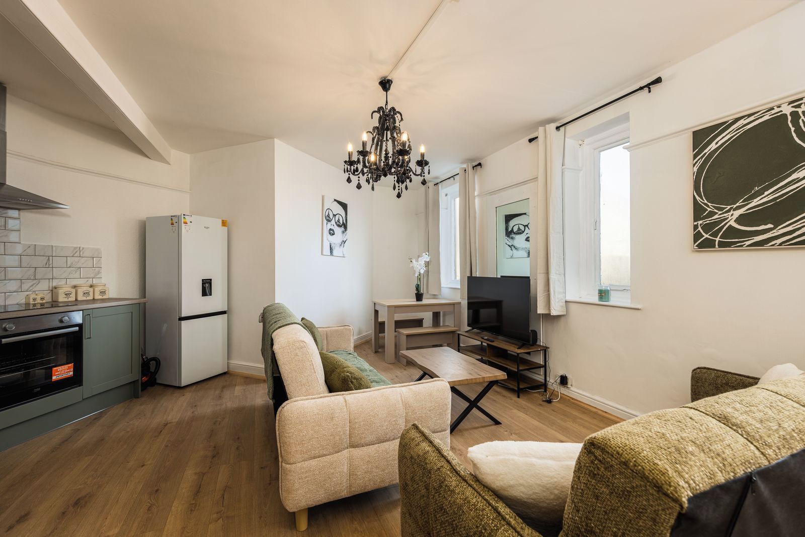 A compact living space with a kitchenette, a sofa set, a dining table, a TV, and artwork on the walls.