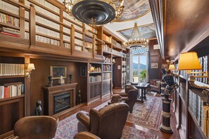 A library with bookshelves, a fireplace, leather chairs, a chandelier, and a view through a window. - Villa Imma in Castellammare di Stabia (Castellammare di Stabia)