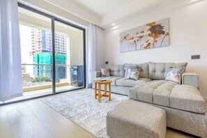 Ein modernes Wohnzimmer mit einem grauen Ecksofa, einem kleinen Holztisch und einem großen Fenster mit Blick auf eine Stadtlandschaft.