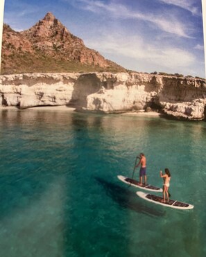 Two people paddleboarding on a calm sea with a rocky coastline in the background. - Villa del Palmar Cabo (San José del Cabo)