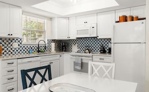 A modern kitchen with white cabinets, a microwave, a refrigerator, and a patterned backsplash. - 5 Stars~WALK TO BEACH from Serendipity Suites! 1-of-2  2-bed/2-ba Cottage Suites (Holmes Beach)
