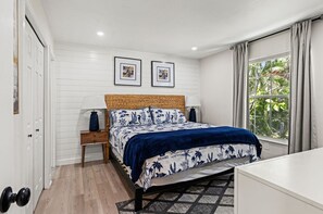 Quarto com cama, mesas de cabeceira, janela com cortinas e porta.