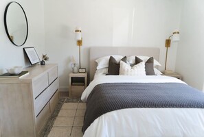 Un dormitorio con cama, mesitas de noche, cómoda y lámparas de pared.