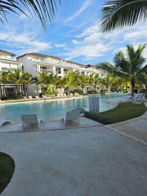 A pool area with lounge chairs and palm trees, surrounded by a building with multiple balconies. - Luxury Penthouse | 2BR | 2 Terraces | Estrrlla Garden Condos (Dominicus)