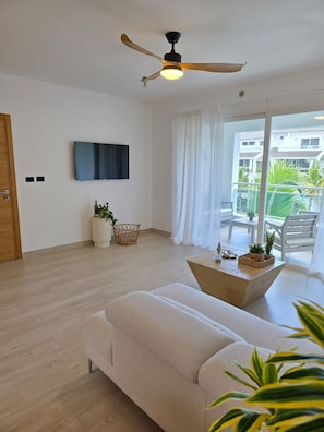 A modern living room with a sofa, a ceiling fan, a flat-screen TV, and a balcony with plants. - Luxury Penthouse | 2BR | 2 Terraces | Estrrlla Garden Condos (Dominicus)