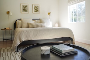 A bedroom with a bed, bedside tables, a bedside lamp, a window, and a tray with books and a candle.