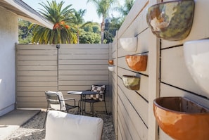 Un espace patio aménagé avec une table et des chaises, un banc rembourré et un mur décoratif orné de bols en céramique.