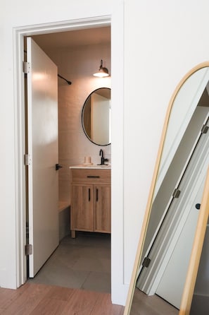 A narrow hallway leading to a bathroom with a wooden cabinet and a round mirror.