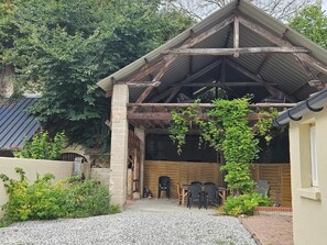 Un espace extérieur aménagé dans un style rustique, avec une pergola en bois, un chemin de gravier et un mur en briques.