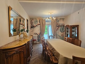 Une salle à manger avec une grande table, des chaises, un lustre et un miroir orné d’une fresque représentant un arbre.